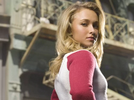 HD desktop wallpaper featuring Hayden Panettiere, showcasing her with long, wavy hair and a casual outfit, captured in an urban setting with elegant architecture in the background.
