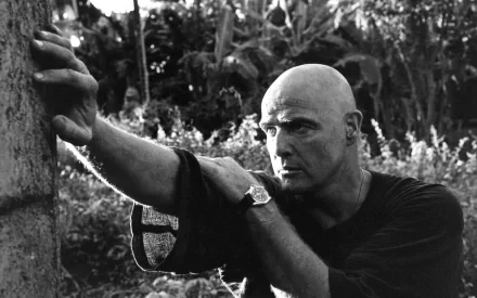 A black and white HD wallpaper from the movie Apocalypse Now, featuring a contemplative figure against a lush background, capturing the film's intense atmosphere.