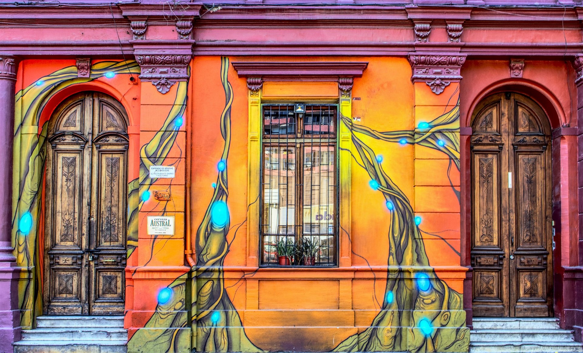 Vibrant man-made facade featuring a colorful orange wall with artistic blue vines, a central window, and two aged wooden doors in 4K Ultra HD detail.