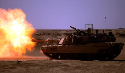 HD desktop wallpaper of an M1 Abrams tank firing in a sandy desert explosion, showcasing military power and armored vehicle strength.