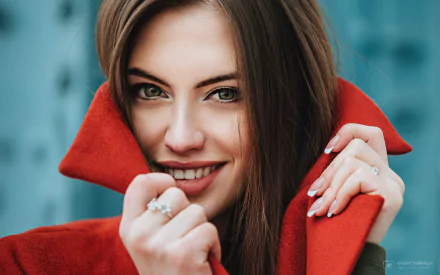 HD desktop wallpaper of a brunette model with brown eyes smiling, showcasing her face framed by a vibrant red coat collar.