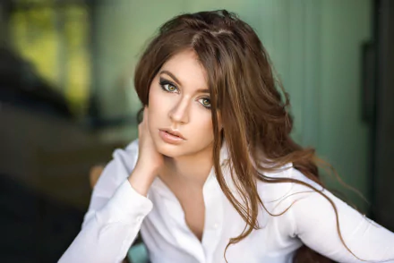 A brunette woman model with long hair gazes thoughtfully, resting her head on her hand, in this HD desktop wallpaper. The background features a soft blur, emphasizing the depth of field effect.