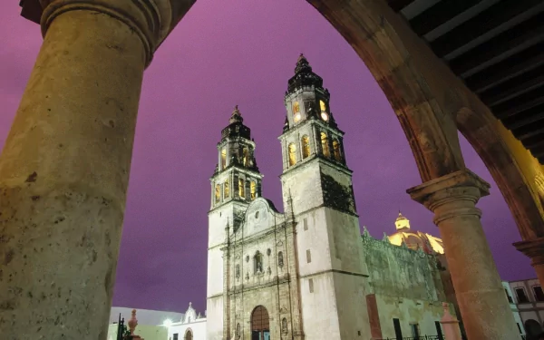 HD wallpaper featuring a stunning Christian cathedral at dusk, framed by historic archways and illuminated under a purple sky.