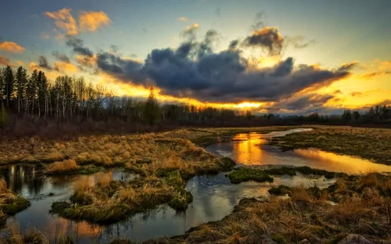A stunning sunset illuminates a tranquil tundra swamp, reflecting vibrant hues on the water, framed by clouds and lush grassland, creating a breathtaking natural landscape.