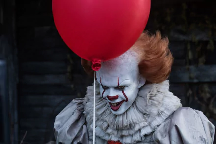 HD desktop wallpaper of Pennywise the clown from the 2017 movie It, holding a red balloon with a menacing smile.