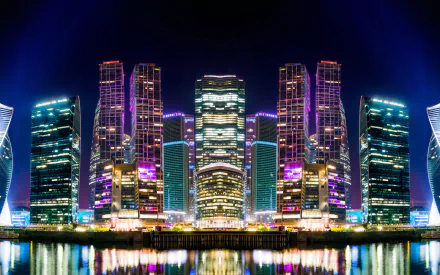 Night view of illuminated skyscrapers reflecting on a river in Moscow, Russia, showcasing vibrant city lights and modern man-made architecture in 4K Ultra HD quality.