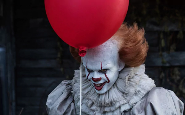 HD desktop wallpaper of Pennywise the clown from the 2017 movie It, holding a red balloon with a menacing smile.