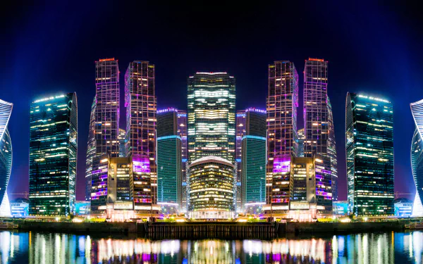 Night view of illuminated skyscrapers reflecting on a river in Moscow, Russia, showcasing vibrant city lights and modern man-made architecture in 4K Ultra HD quality.