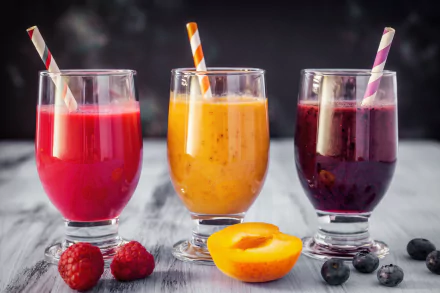 Three glasses of vibrant apricot, blueberry, and raspberry smoothies with striped straws, surrounded by fresh fruit, captured in an 8K Ultra HD desktop wallpaper.