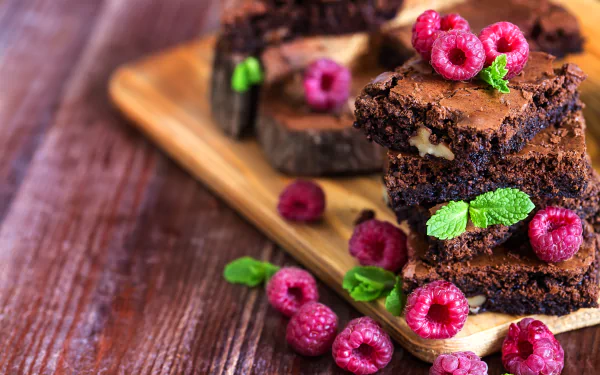 Close-up of rich chocolate brownies topped with fresh raspberries and mint leaves on a wooden board, captured in stunning 4K Ultra HD for a vibrant dessert wallpaper.