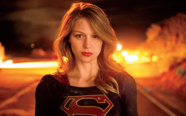 Melissa Benoist as Supergirl stands confidently against a fiery background, showcasing her iconic superhero persona in this HD wallpaper from the TV show Supergirl.