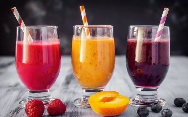 Three glasses of vibrant apricot, blueberry, and raspberry smoothies with striped straws, surrounded by fresh fruit, captured in an 8K Ultra HD desktop wallpaper.