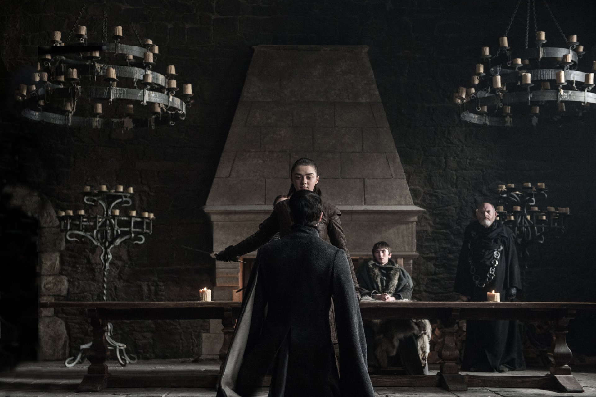 4K Ultra HD Game of Thrones TV show desktop wallpaper: dim Great Hall with three figures at a long table — a cloaked figure in foreground and two others beneath candlelit chandeliers.