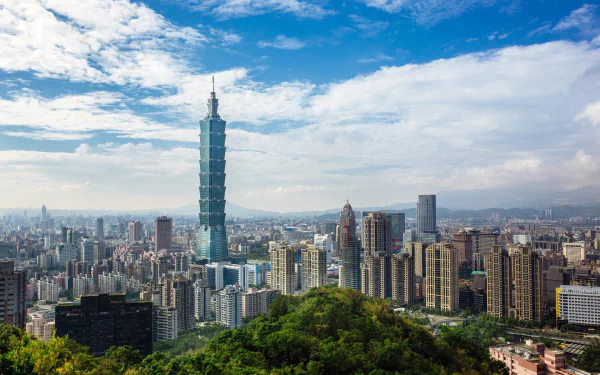 HD cityscape wallpaper featuring Taipei 101 skyscraper towering over Taipei, Taiwan, with a bright sky and scattered clouds above the urban skyline.