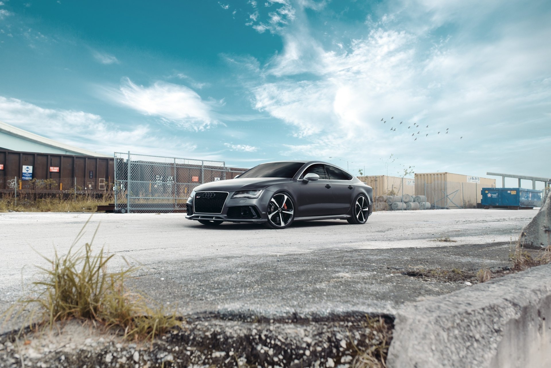 Silver Audi RS7 parked in an industrial lot under a dramatic blue sky — HD PC desktop wallpaper/background showcasing the sleek performance vehicle.
