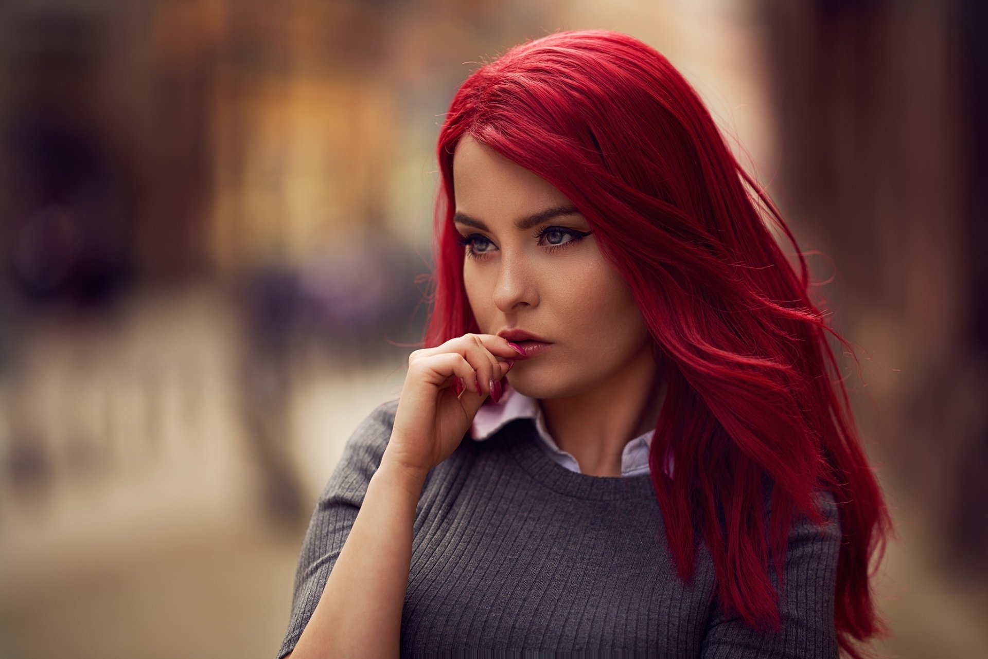 HD desktop wallpaper featuring a model with blue eyes and vibrant red hair, standing in a depth-of-field blurred background, wearing a gray sweater.