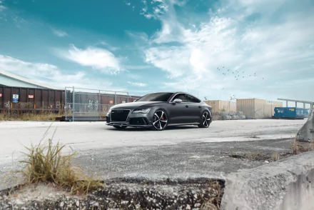 Silver Audi RS7 parked in an industrial lot under a dramatic blue sky — HD PC desktop wallpaper/background showcasing the sleek performance vehicle.