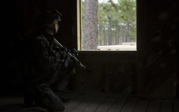 HD desktop wallpaper showing a soldier holding an M4 Carbine assault rifle inside a dark military outpost, with a forest visible through the window.
