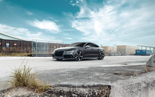 Silver Audi RS7 parked in an industrial lot under a dramatic blue sky — HD PC desktop wallpaper/background showcasing the sleek performance vehicle.