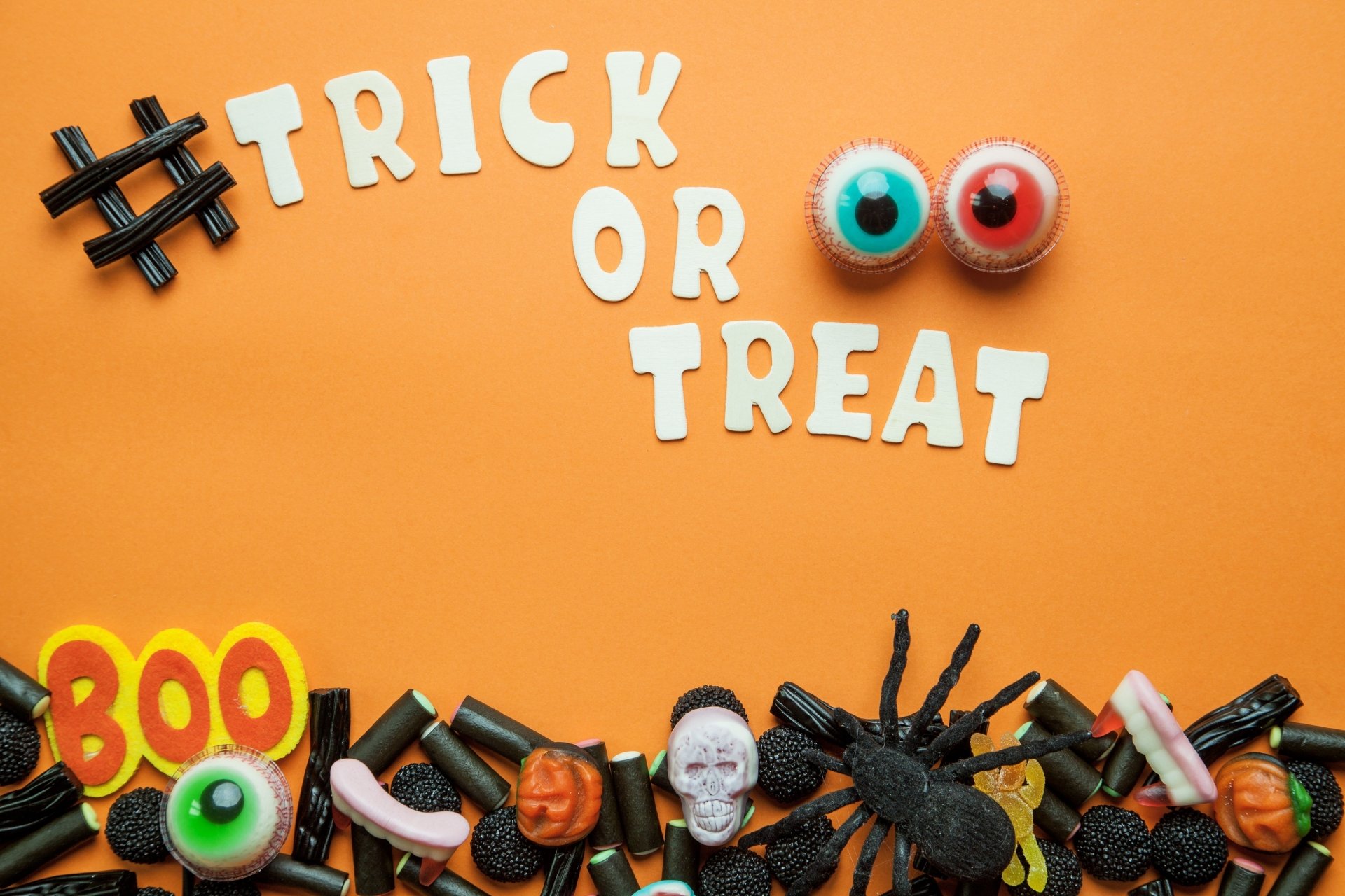 HD Halloween desktop wallpaper featuring Trick or Treat text, colorful candy eyes, and assorted spooky sweets like spiders and skulls on an orange background.