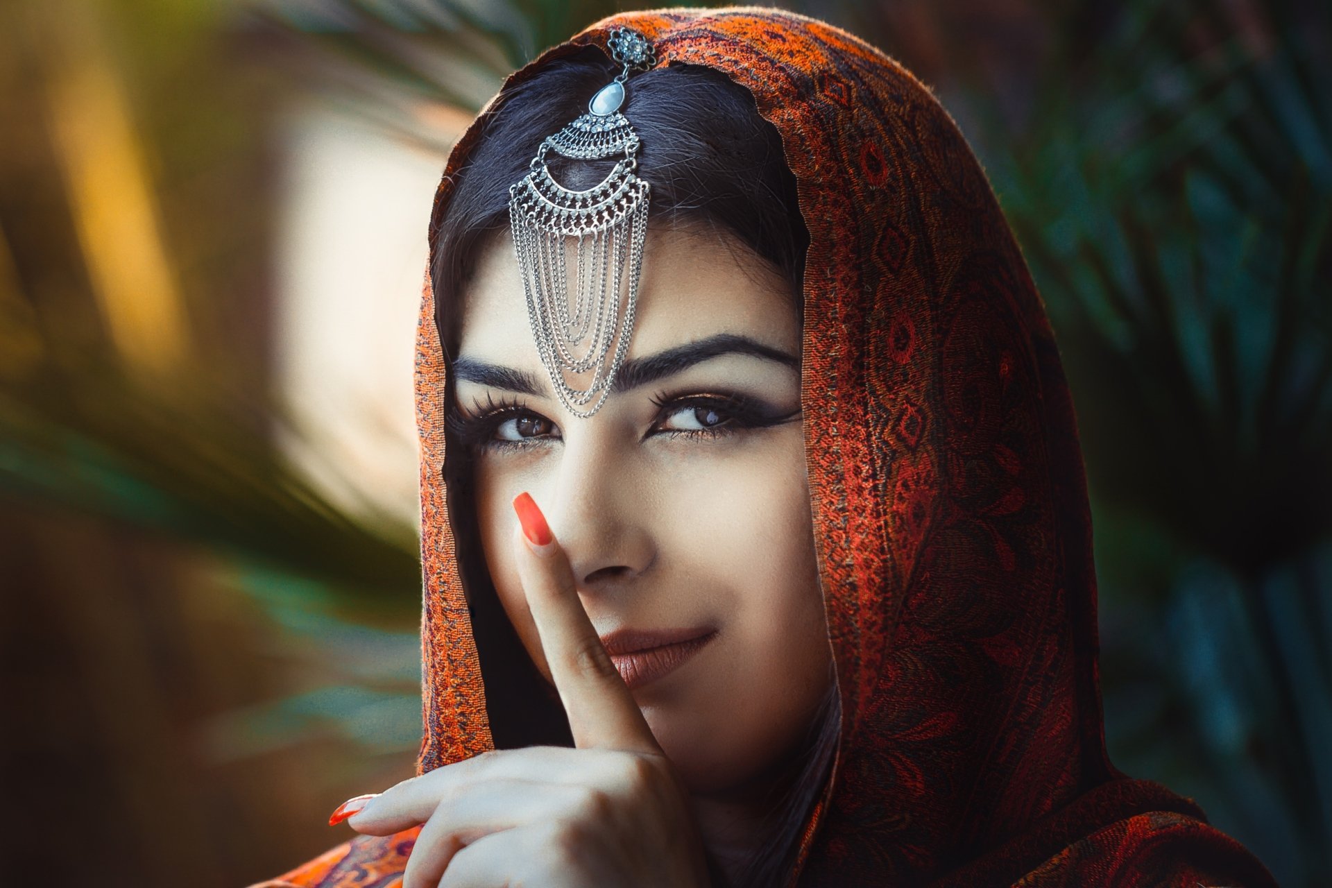 HD desktop wallpaper featuring a brunette woman with brown eyes wearing a saree and traditional headpiece, posing with a finger to her lips. Perfectly captures serene beauty and cultural elegance.