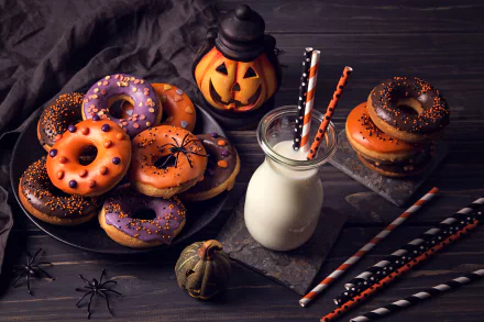 Halloween-themed HD wallpaper featuring a plate of colorful doughnuts, a bottle of milk with straws, and festive decorations including a pumpkin lantern and toy spiders.