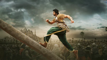 A dynamic HD desktop wallpaper from the movie Baahubali 2: The Conclusion, featuring a warrior running up a wooden structure with a castle and battlefield in the background.