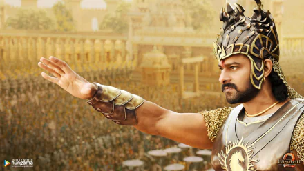 A HD desktop wallpaper from the movie Baahubali 2: The Conclusion, featuring a regal character in ornate armor extending his arm, with a large crowd and grand architecture in the background.