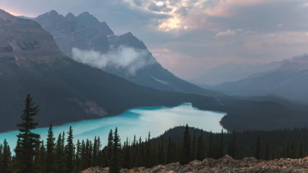 HD desktop wallpaper showcasing the serene landscape of Banff National Park, Canada, with a turquoise lake surrounded by forested mountains under a cloudy sky.