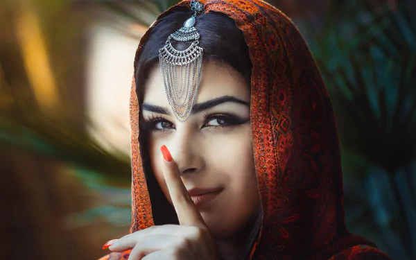 HD desktop wallpaper featuring a brunette woman with brown eyes wearing a saree and traditional headpiece, posing with a finger to her lips. Perfectly captures serene beauty and cultural elegance.