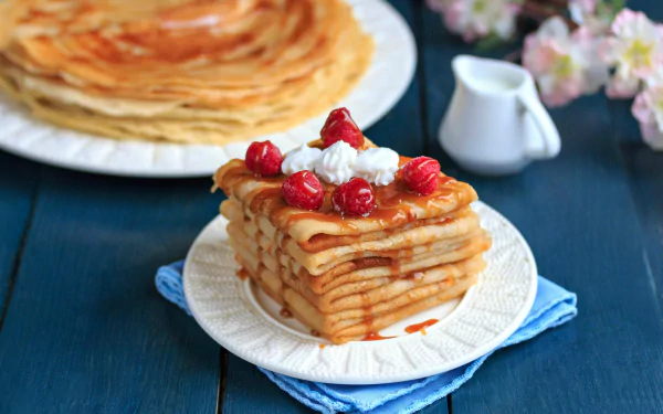 HD desktop wallpaper featuring a stack of layered crêpes topped with whipped cream and red berries on a white plate, with more crêpes and a small pitcher in the background.