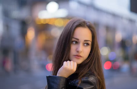 Portrait of a brunette model with hazel eyes and contemplative expression, face in sharp focus against bokeh city lights and shallow depth of field — 5K Ultra HD PC desktop wallpaper/background.
