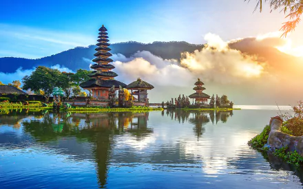 HD desktop wallpaper showcasing the serene reflection of Pura Ulun Danu Bratan temple on a lake in Indonesia, surrounded by misty mountains and a glowing sunrise.