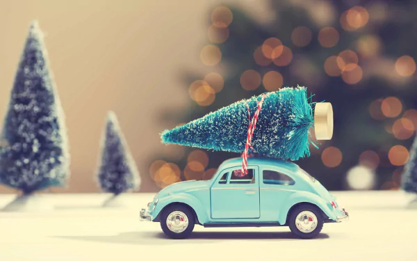 A toy car carrying a miniature Christmas tree with holiday bokeh lights in the background, presented as an HD PC desktop wallpaper and background.