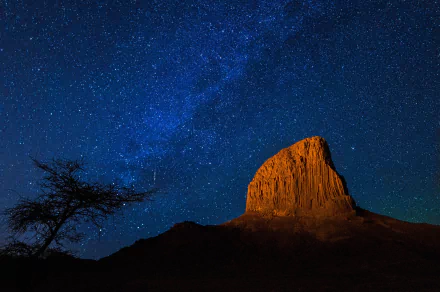 HD desktop wallpaper depicting the stunning Milky Way above the Hoggar Mountains in the Sahara Desert, Tassili N'Ajjer, Algeria. The majestic night sky enhances the rugged beauty of this African landscape.