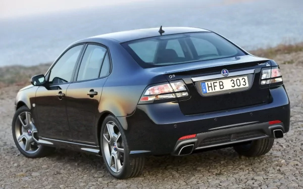 HD PC desktop wallpaper background of a dark Saab sedan (car/vehicle) parked on a rocky shore, rear three-quarter view highlighting taillights, alloy wheels and license plate HFB 303.