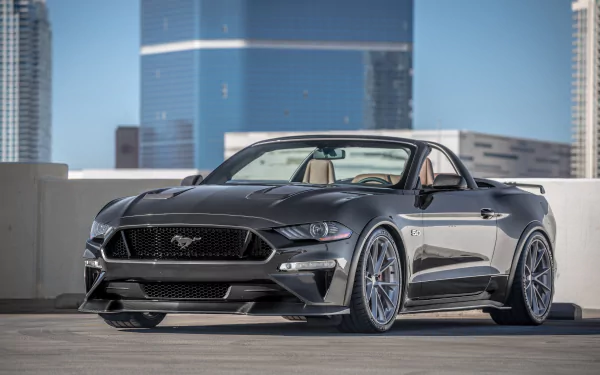 A high-definition desktop wallpaper featuring a sleek silver Ford Mustang muscle car parked in an urban setting, with modern buildings in the background.