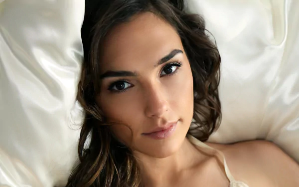 HD desktop wallpaper featuring Israeli actress and model Gal Gadot, showcasing her brunete hair and brown eyes as she lies against a silky background.