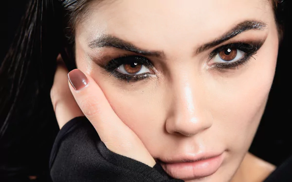 Close-up 4K Ultra HD image of a woman model with striking brown eyes, intense gaze, and flawless makeup, set against a dark background.