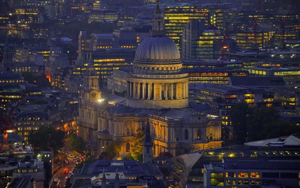 Night view of St Paul's Cathedral dome illuminated amidst the cityscape of London, England, showcasing the religious landmark surrounded by urban buildings.