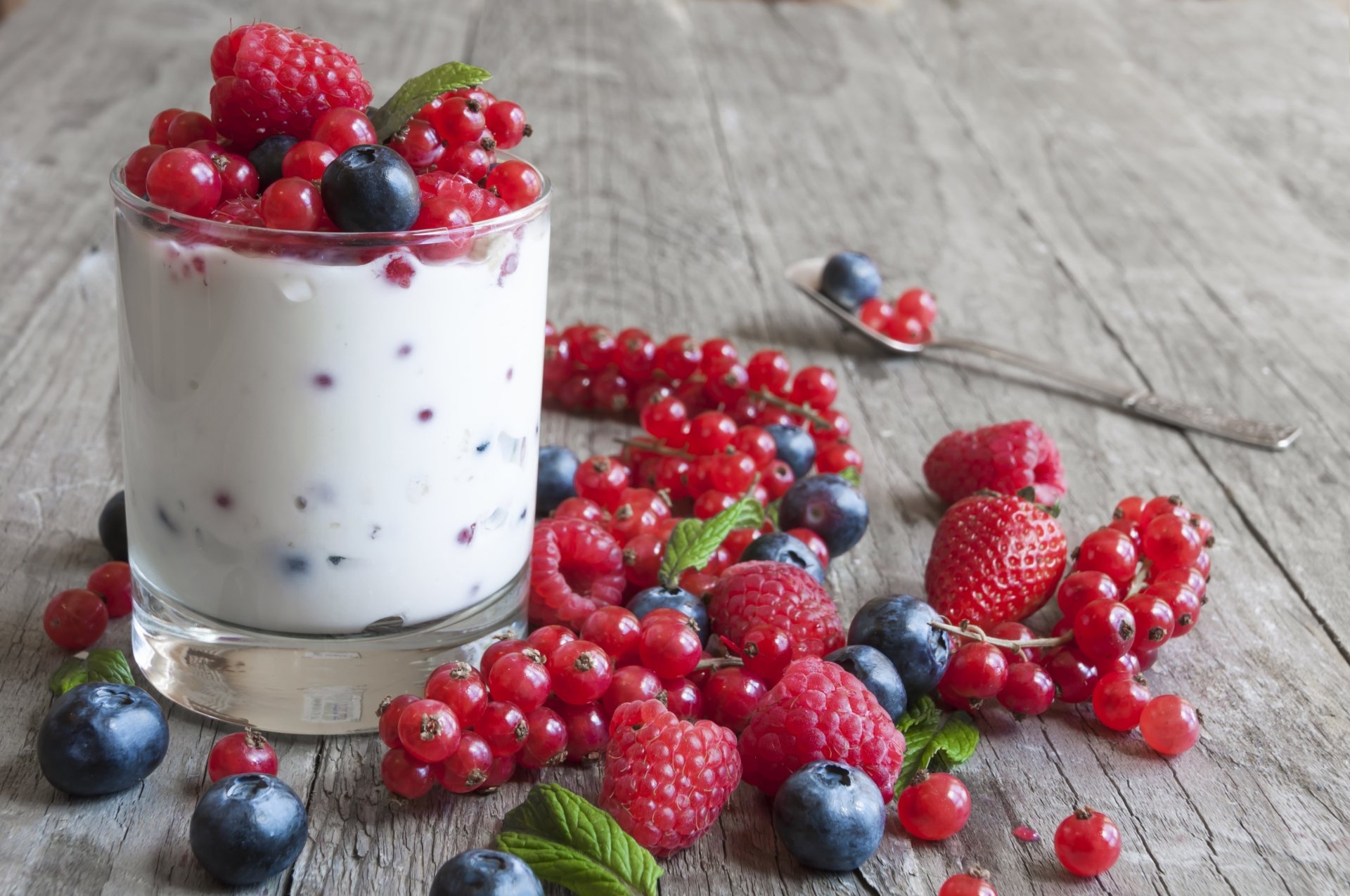 4K Ultra HD PC desktop wallpaper background still life: glass of yogurt topped with raspberries, blueberries and red currants, scattered fruit and mint on a rustic wooden surface.