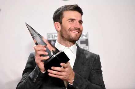 Sam Hunt smiles while holding a trophy, dressed in a stylish suit against a simple background. This HD wallpaper captures his success in the music industry.