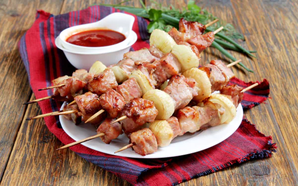 Plate of grilled meat kebabs with onions and a side of ketchup on a red cloth, captured in high-definition for a barbecue-themed PC desktop wallpaper.