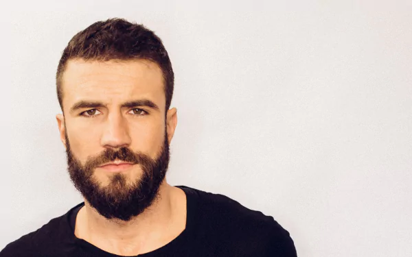 HD desktop wallpaper featuring a portrait of a bearded man in a black shirt against a light background.