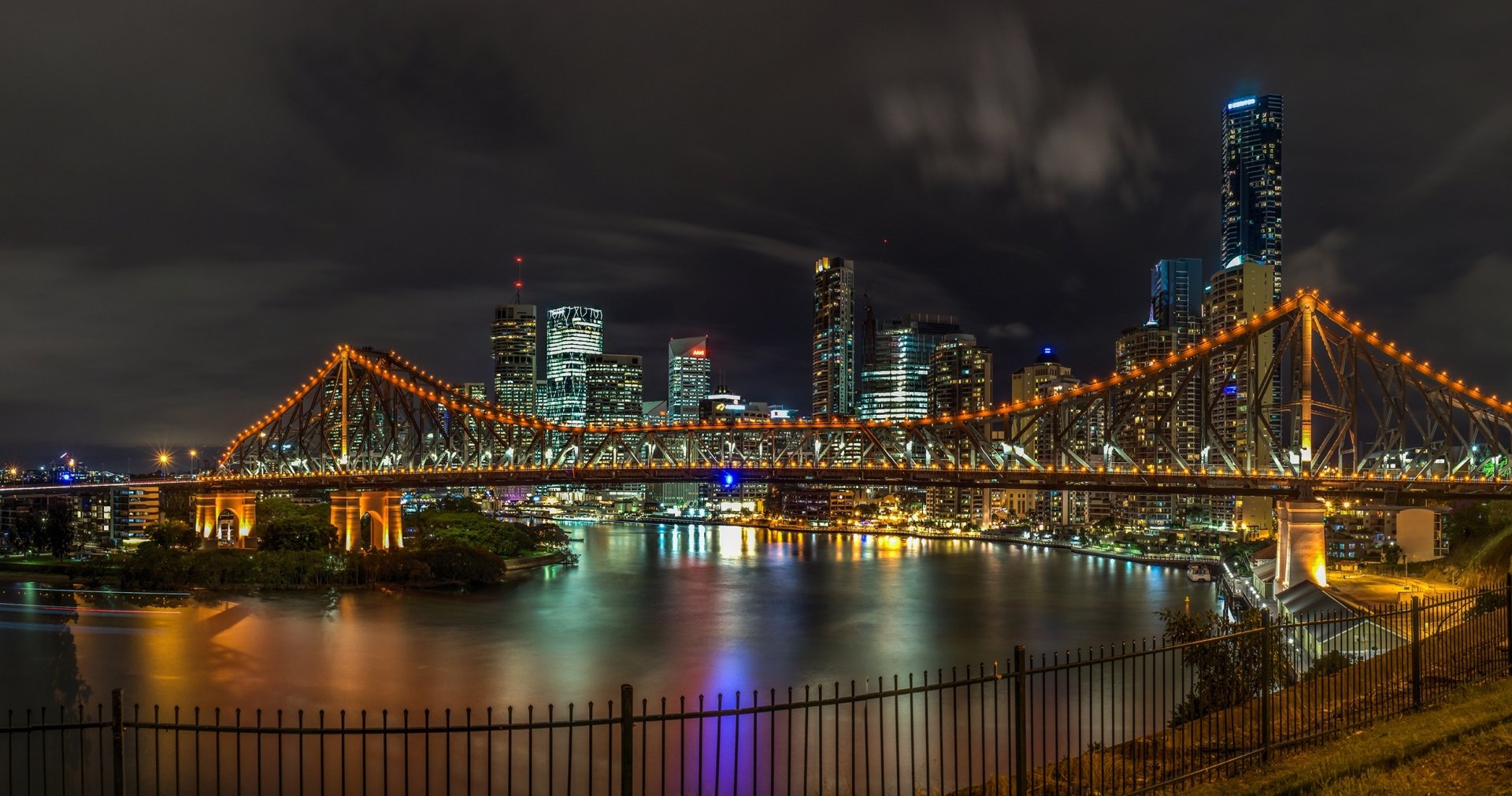 Night view of Brisbane’s Story Bridge illuminated with orange lights, spanning the river against a backdrop of skyscrapers and city buildings in Australia.