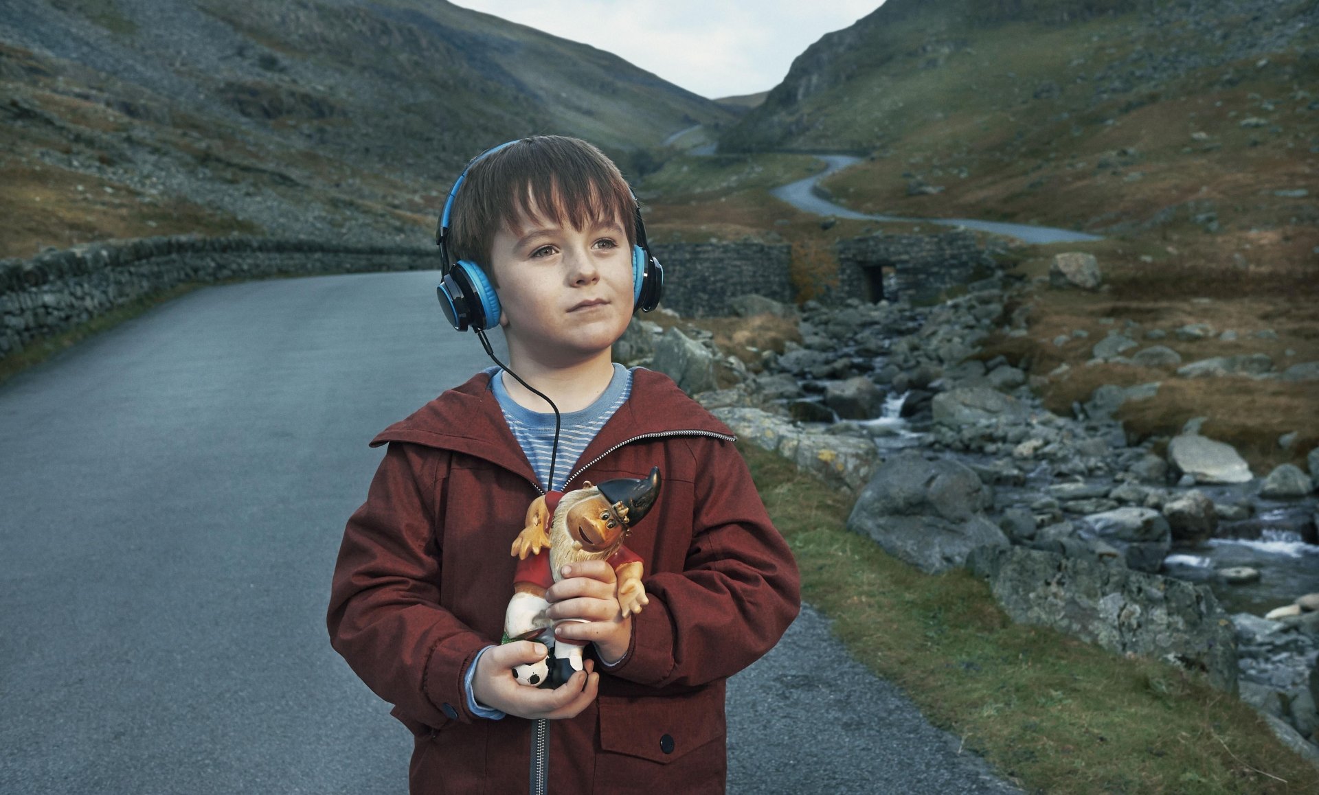 HD desktop wallpaper from The A Word featuring a young boy with headphones standing on a road amidst a hilly landscape.
