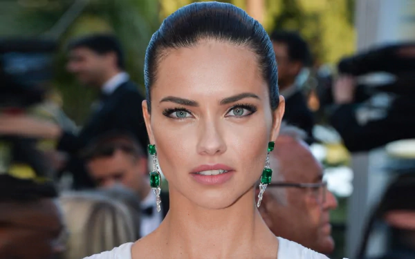 Close-up portrait of a blue-eyed Brazilian model with emerald drop earrings, sleek pulled-back hair and poised expression, 4K Ultra HD PC desktop wallpaper.