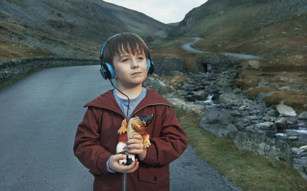 HD desktop wallpaper from The A Word featuring a young boy with headphones standing on a road amidst a hilly landscape.