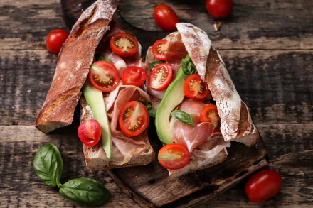 HD desktop wallpaper showing a still life of a sandwich with fresh bread, tomato slices, ham, and basil on a rustic wooden surface.