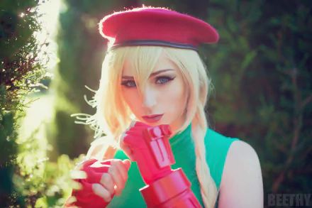HD PC wallpaper of a woman cosplaying as Cammy from Street Fighter, wearing a red beret and red gloves with a green outfit, set against a blurred outdoor background.